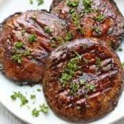 Grilled portobello mushrooms are served on a white plate.
