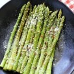 Roasted asparagus is topped with Parmesan and served on a dark plate.
