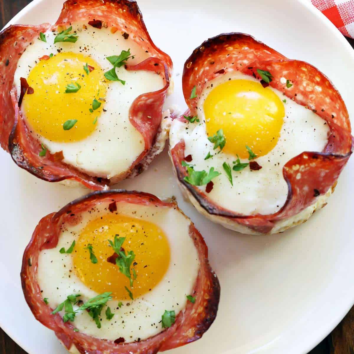 Salami and egg cups are served on a white plate.