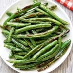 Roasted green beans are served on a white plate with a napkin.