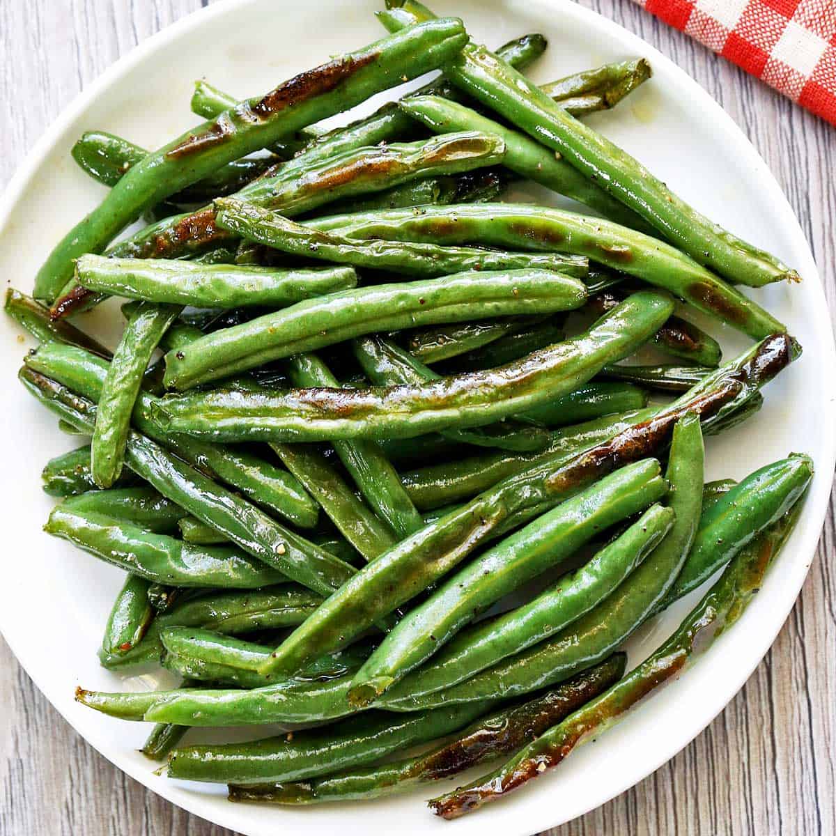 Roasted green beans are served on a white plate with a napkin.