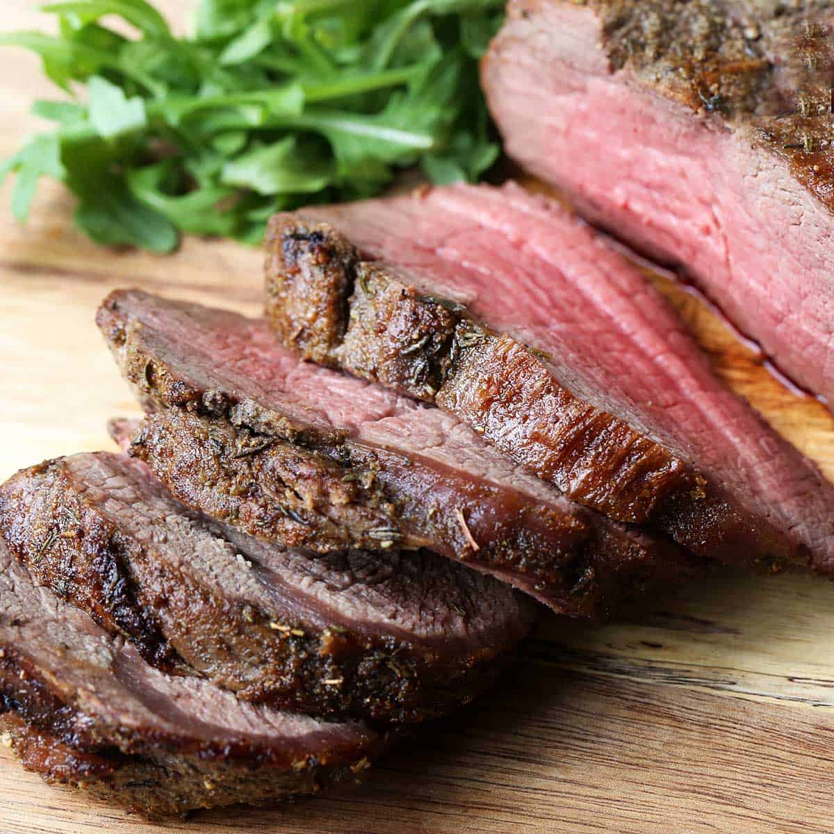 A sliced beef tenderloin roast is served on a wooden cutting board.