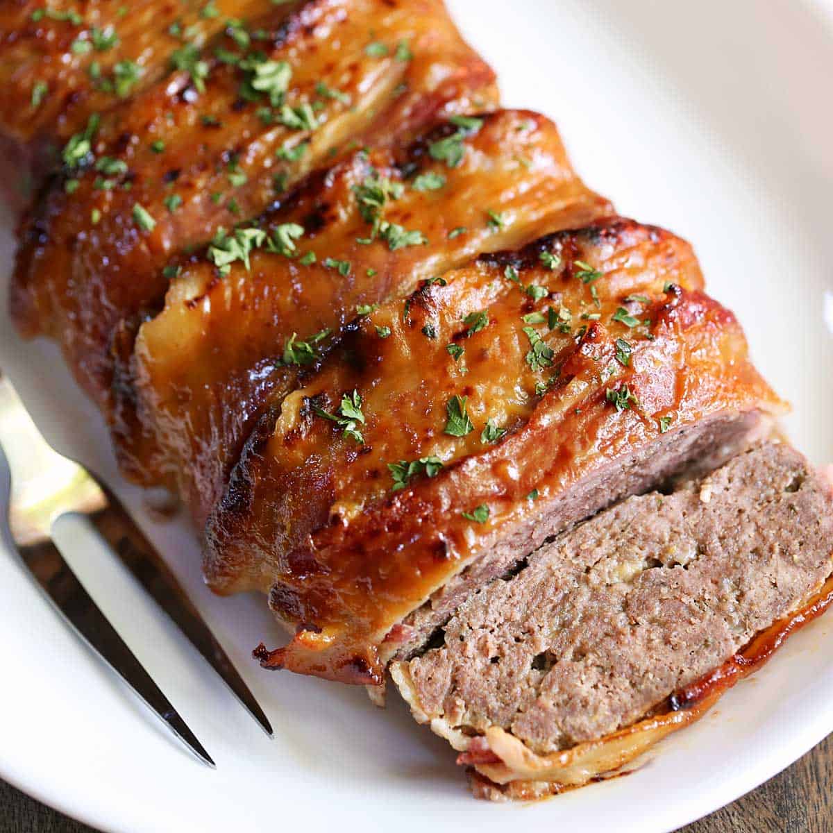 Bacon wrapped meatloaf, sliced, is served on a white plate.
