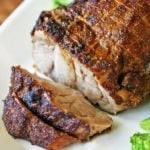 Pork roast is served on a white platter with broccoli.