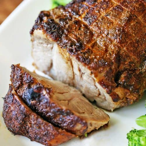 Pork roast is served on a white platter with broccoli.