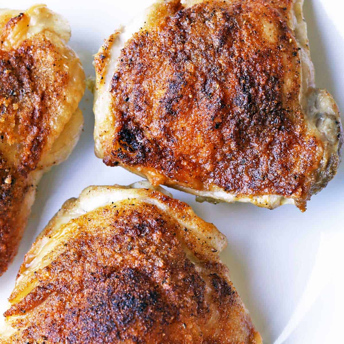 Crispy chicken thighs are served on a white plate.