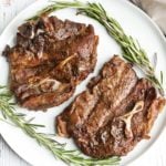 Lamb shoulder chops are served on a white plate with a garnish of rosemary.