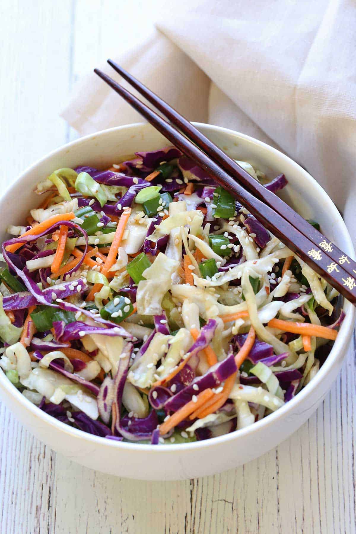 Asian cabbage salad is served in a white bowl with chopsticks. 
