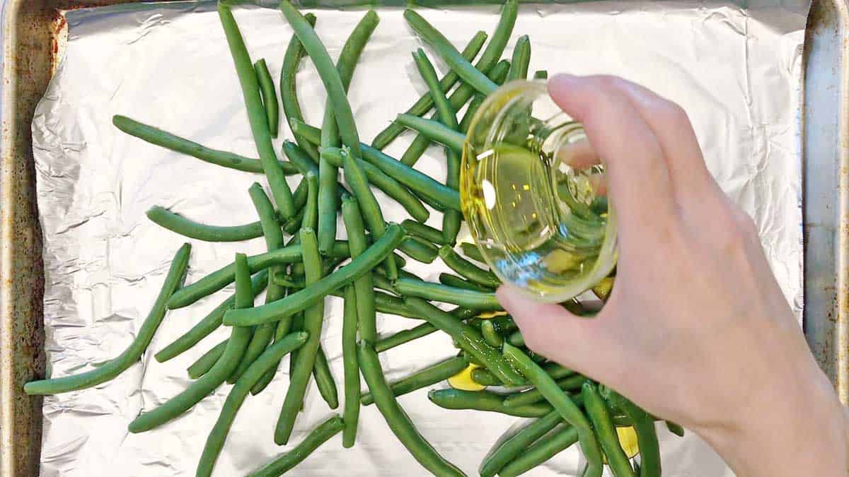 Coating green beans in olive oil.