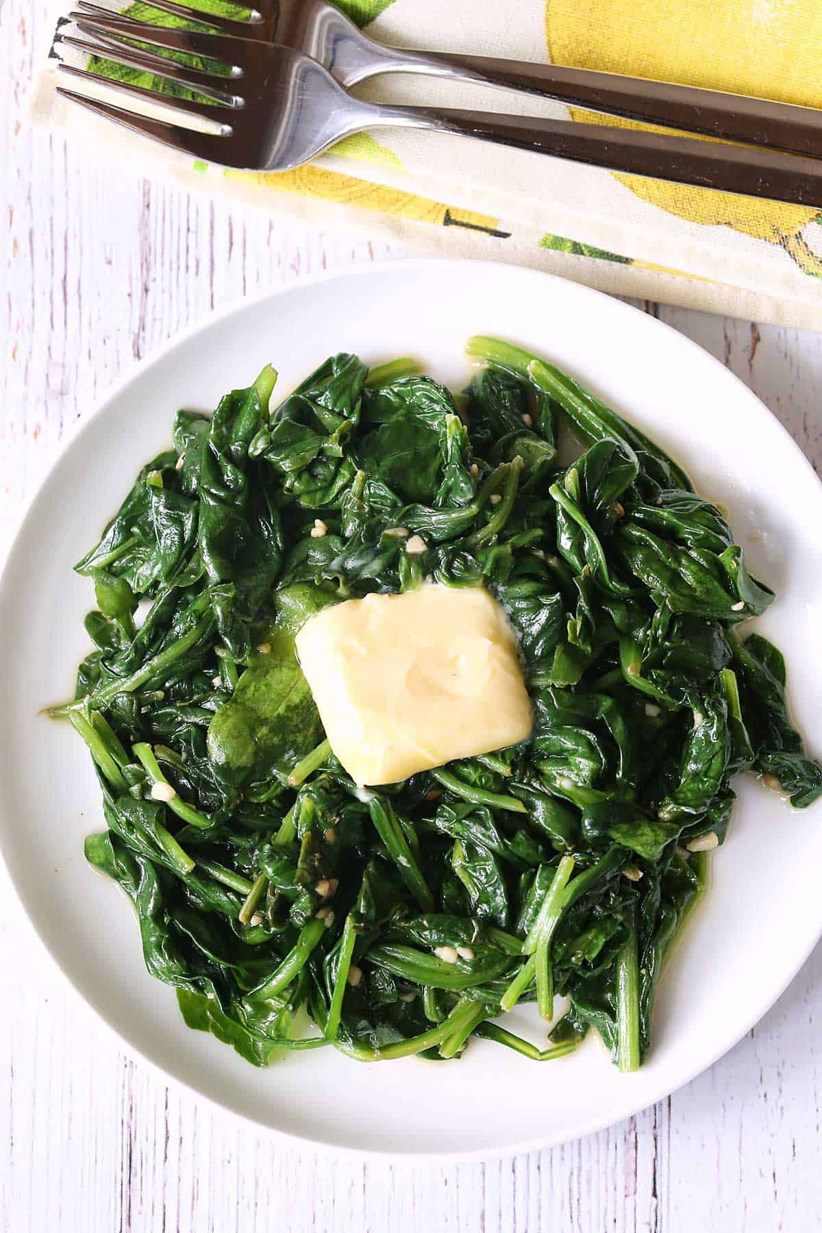 Sauteed spinach is topped with butter and served on a white plate.