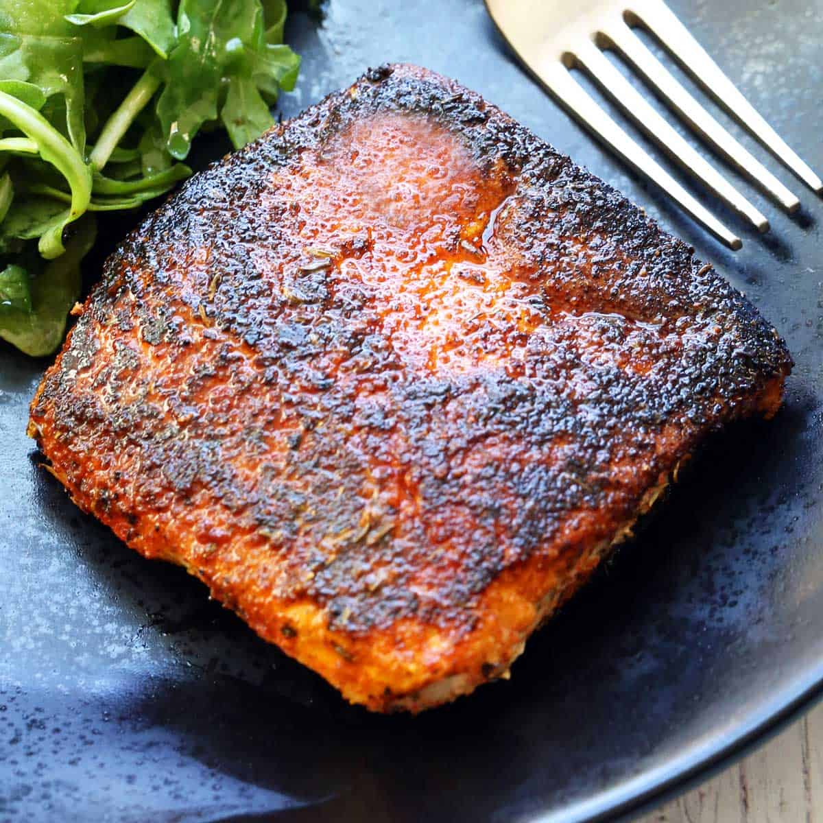 Blackened halibut is served on a dark plate.