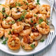 Garlic butter shrimp are served on a white plate with a fork.