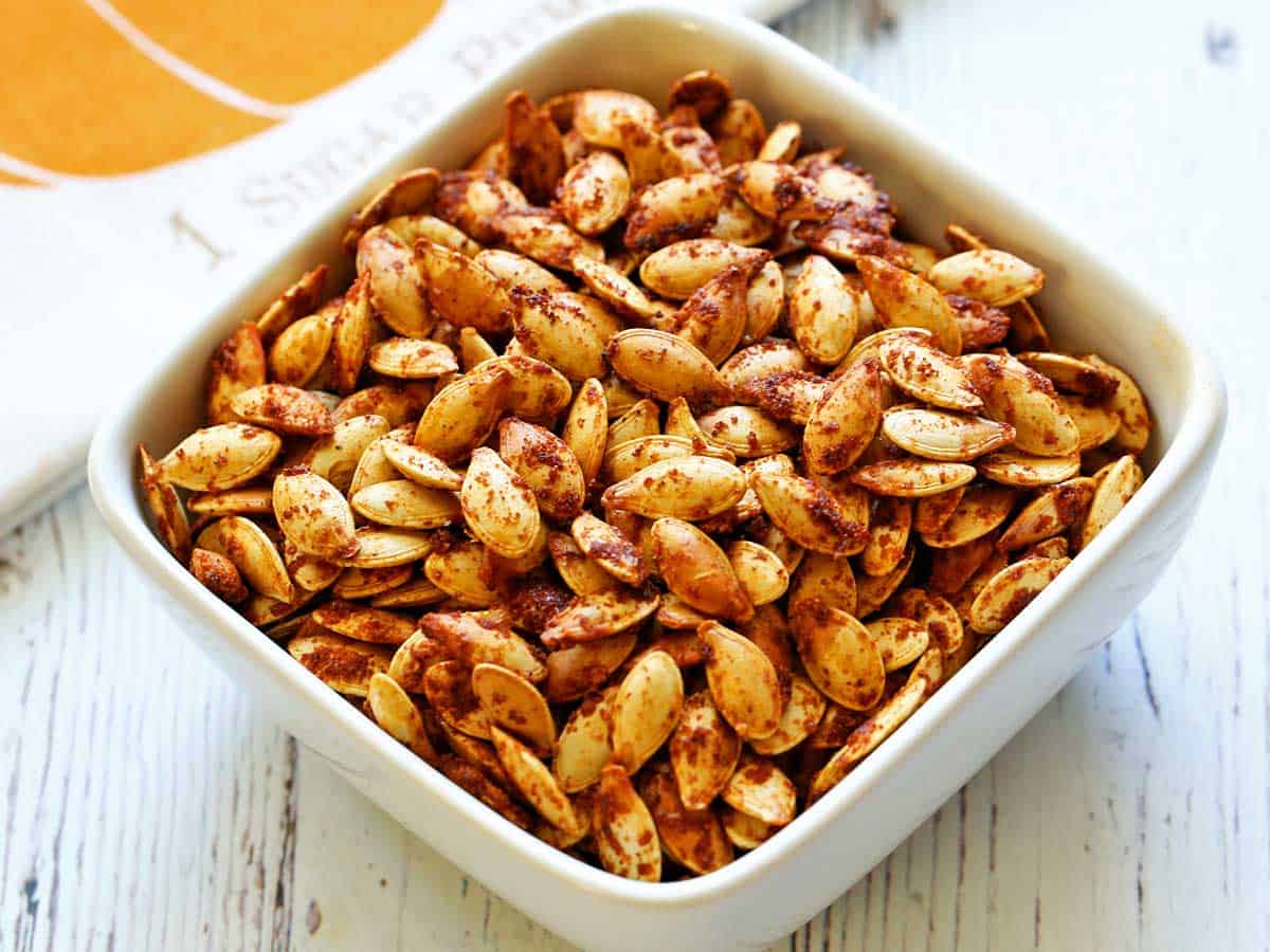 Roasted pumpkin seeds are served in a white bowl. 
