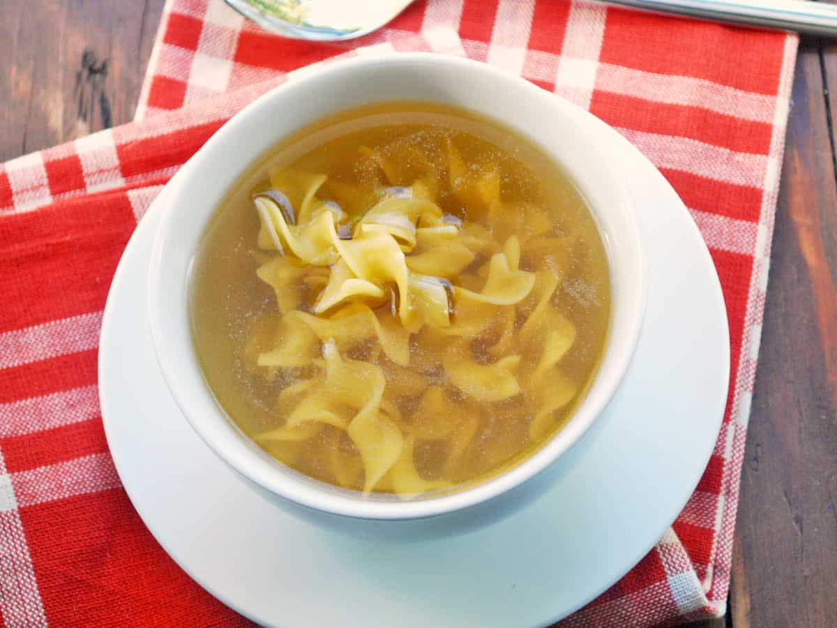 Chicken noodle soup served in a white bowl with a red napkin.