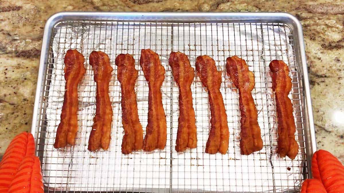 Baked slices of bacon on a rack inside a baking sheet.