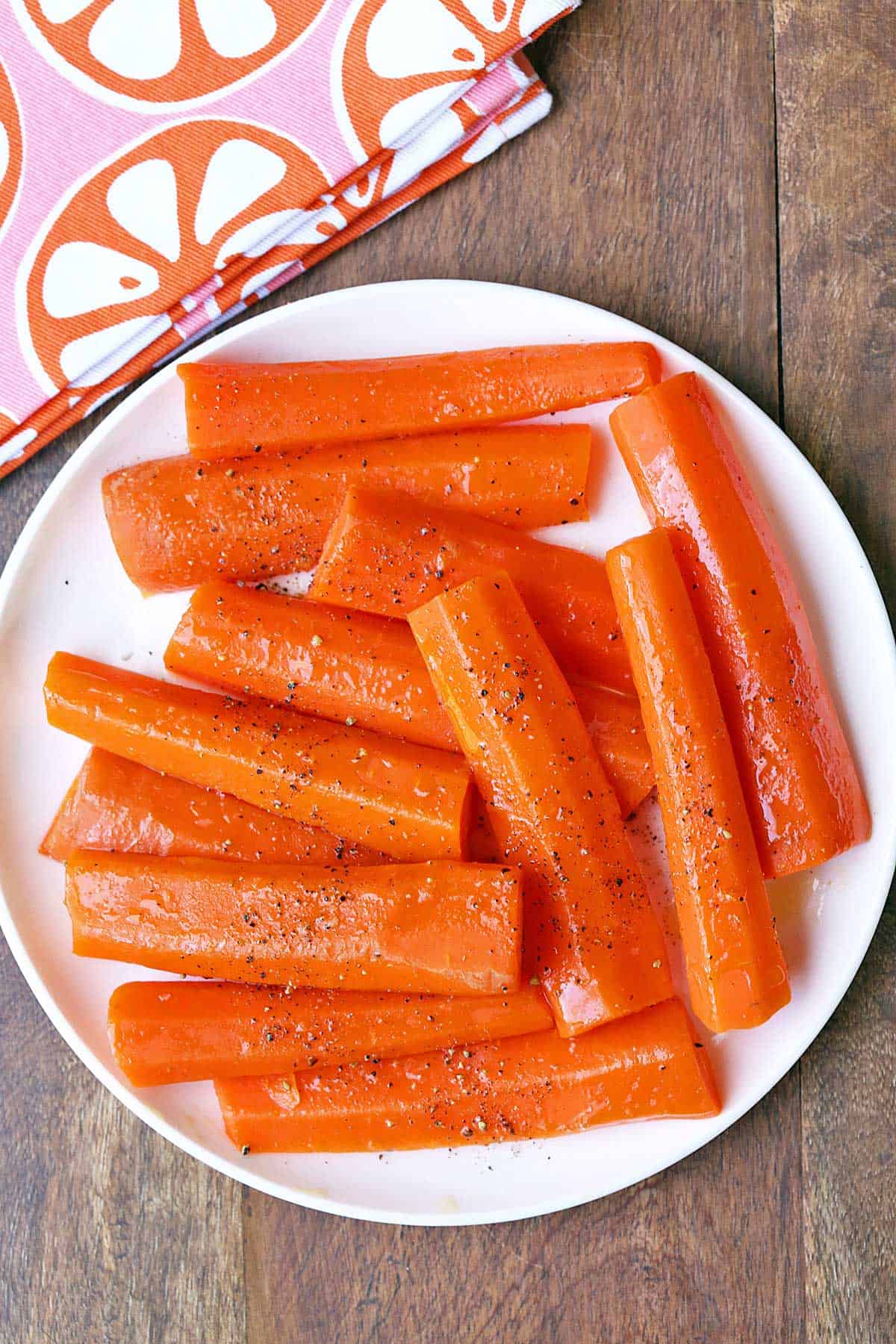 Steamed carrots are served on a white plate with a napkin. 