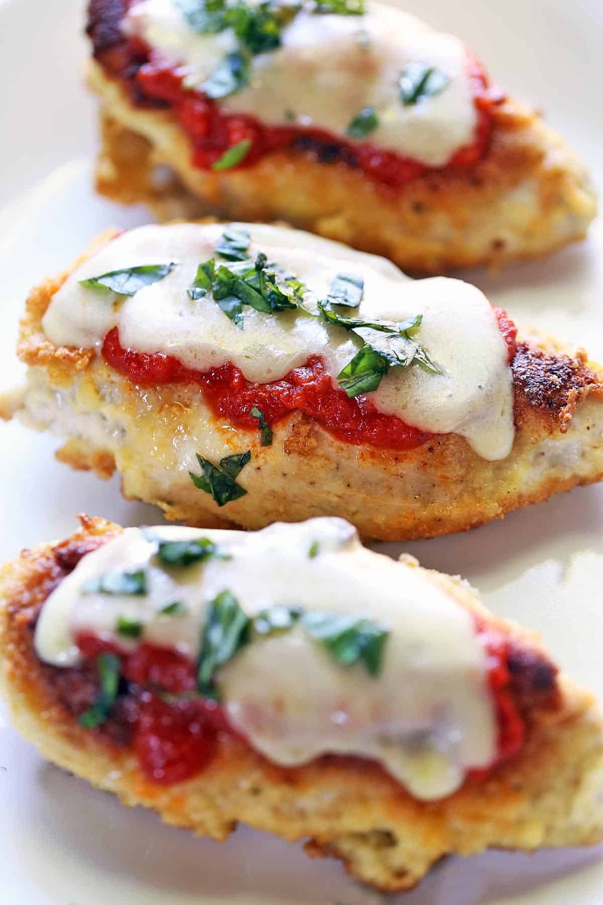 Three pieces of keto chicken Parmesan are served on a white plate. 