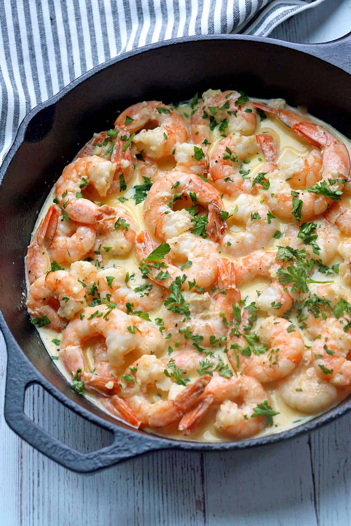 Shrimp in cream sauce are served in a skillet and topped with parsley. 