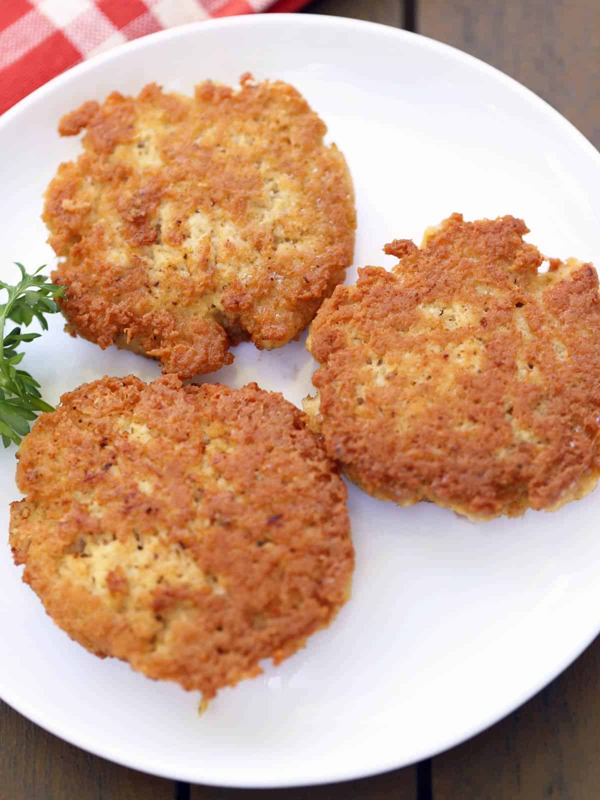Three chicken patties are served on a white plate with a red napkin. 