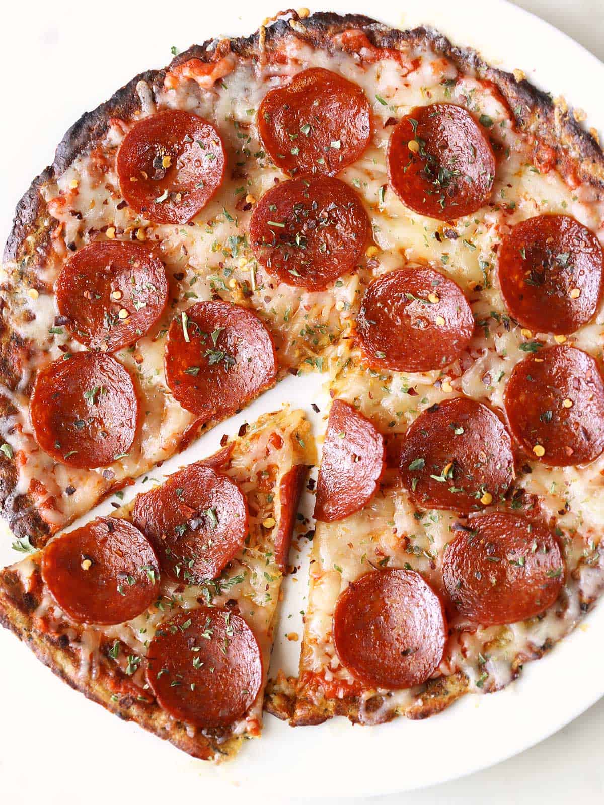 Pizza made with a cauliflower crust is served on a white plate. 