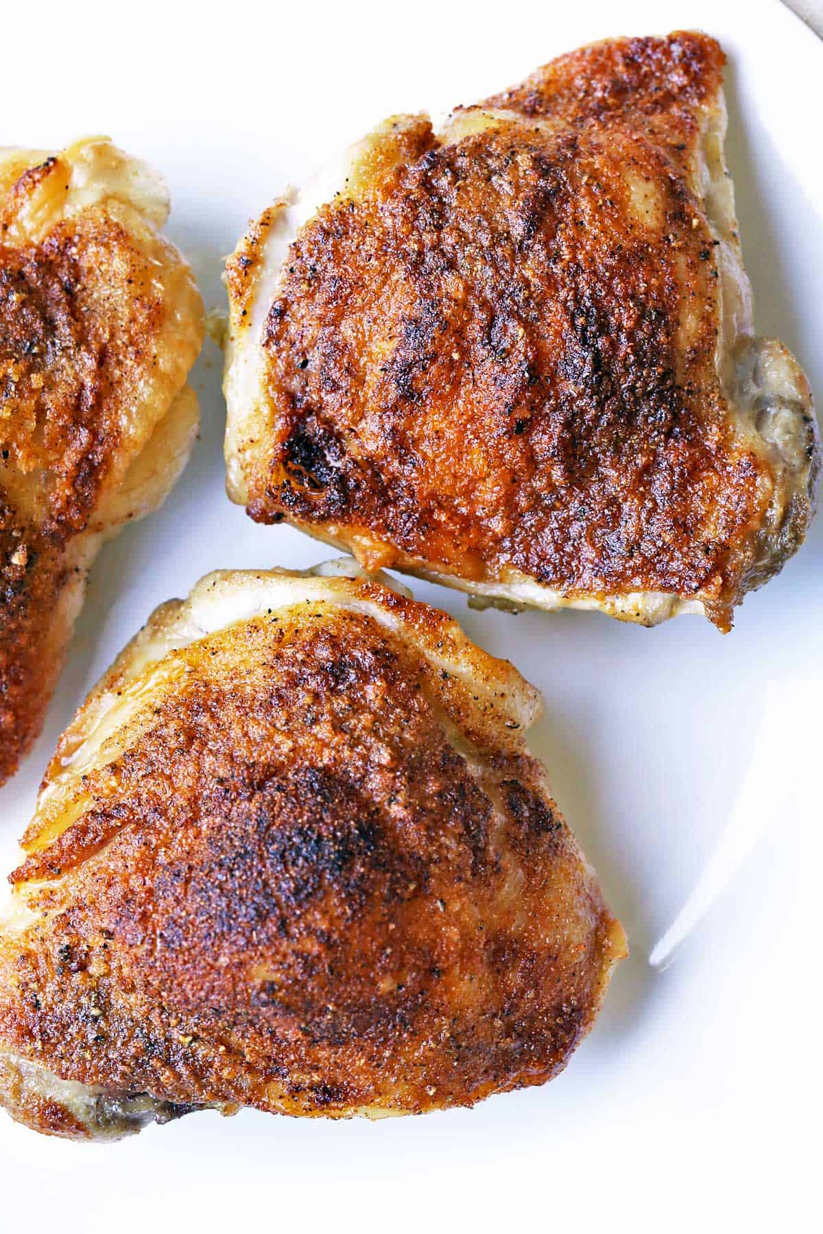 Three crispy chicken thighs on a plate.