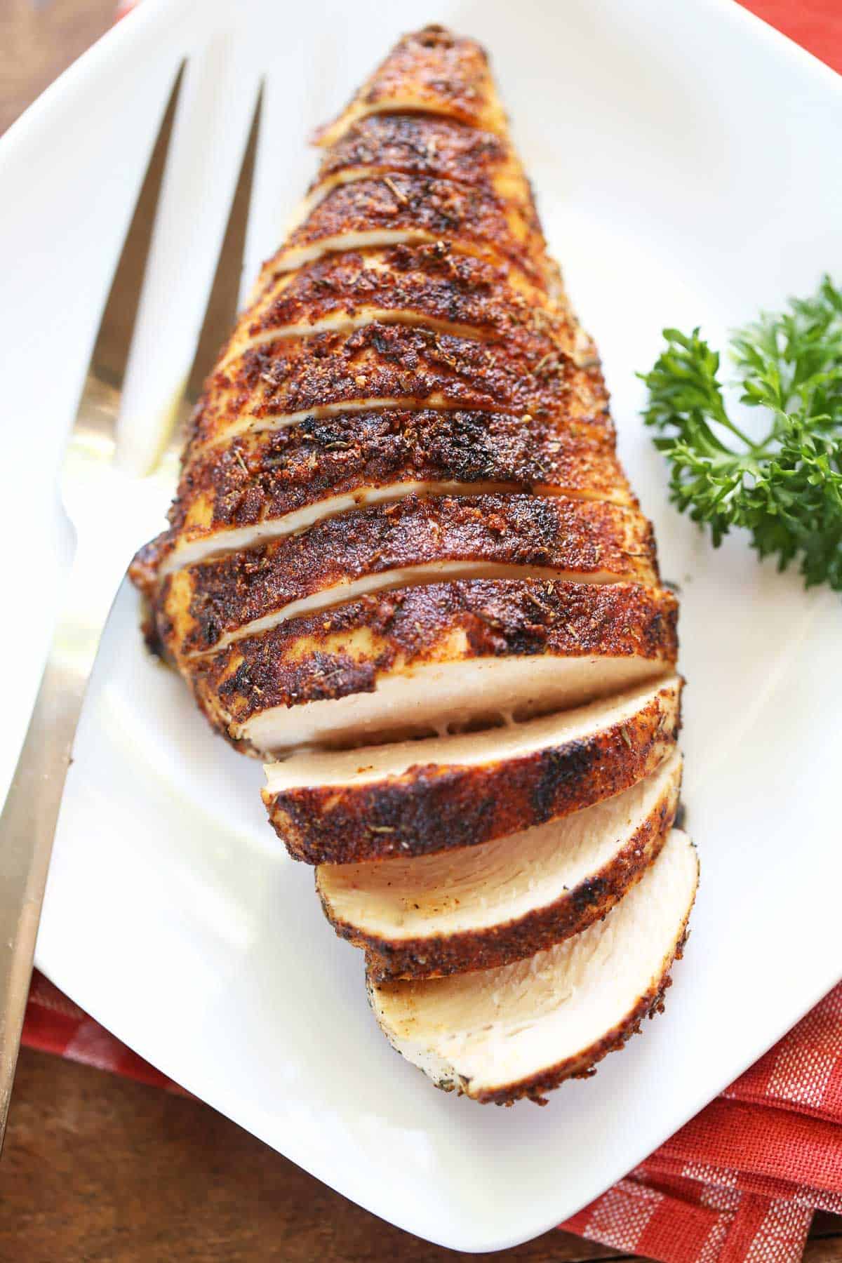 Blackened chicken is served on a white plate with a serving fork. 