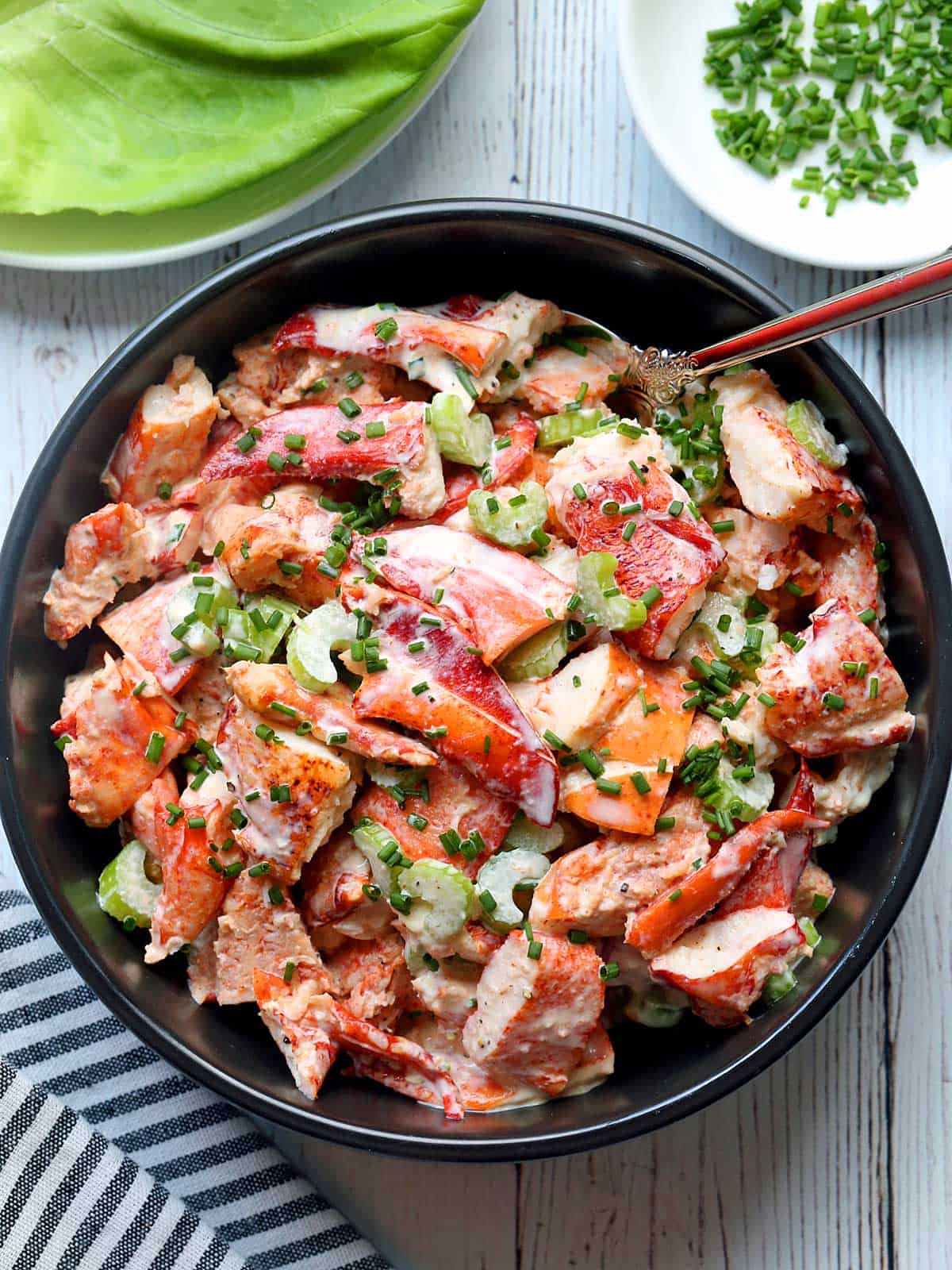 Lobster salad served in a black bowl with lettuce leaves and chives. 