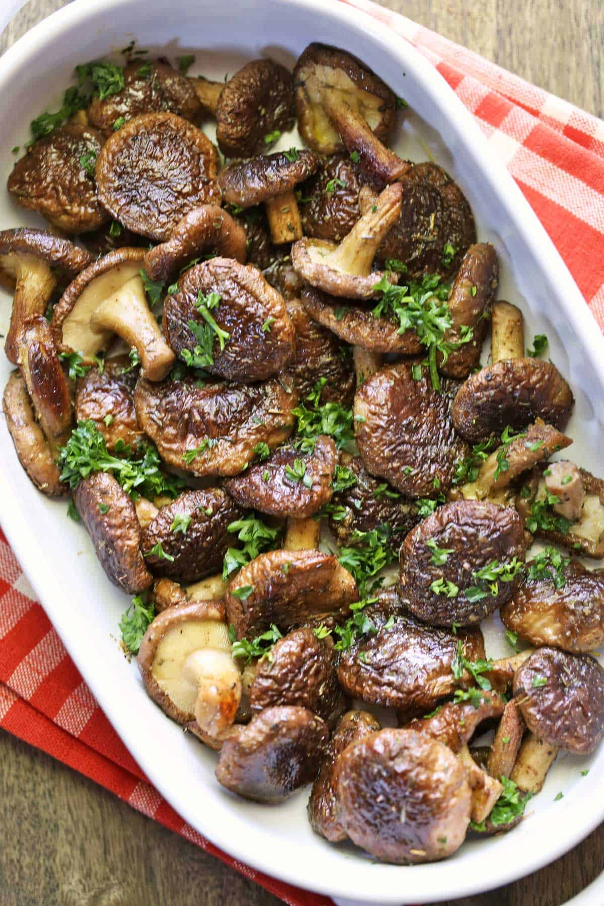 Shiitake mushrooms are served in a white dish and topped with parsley. 
