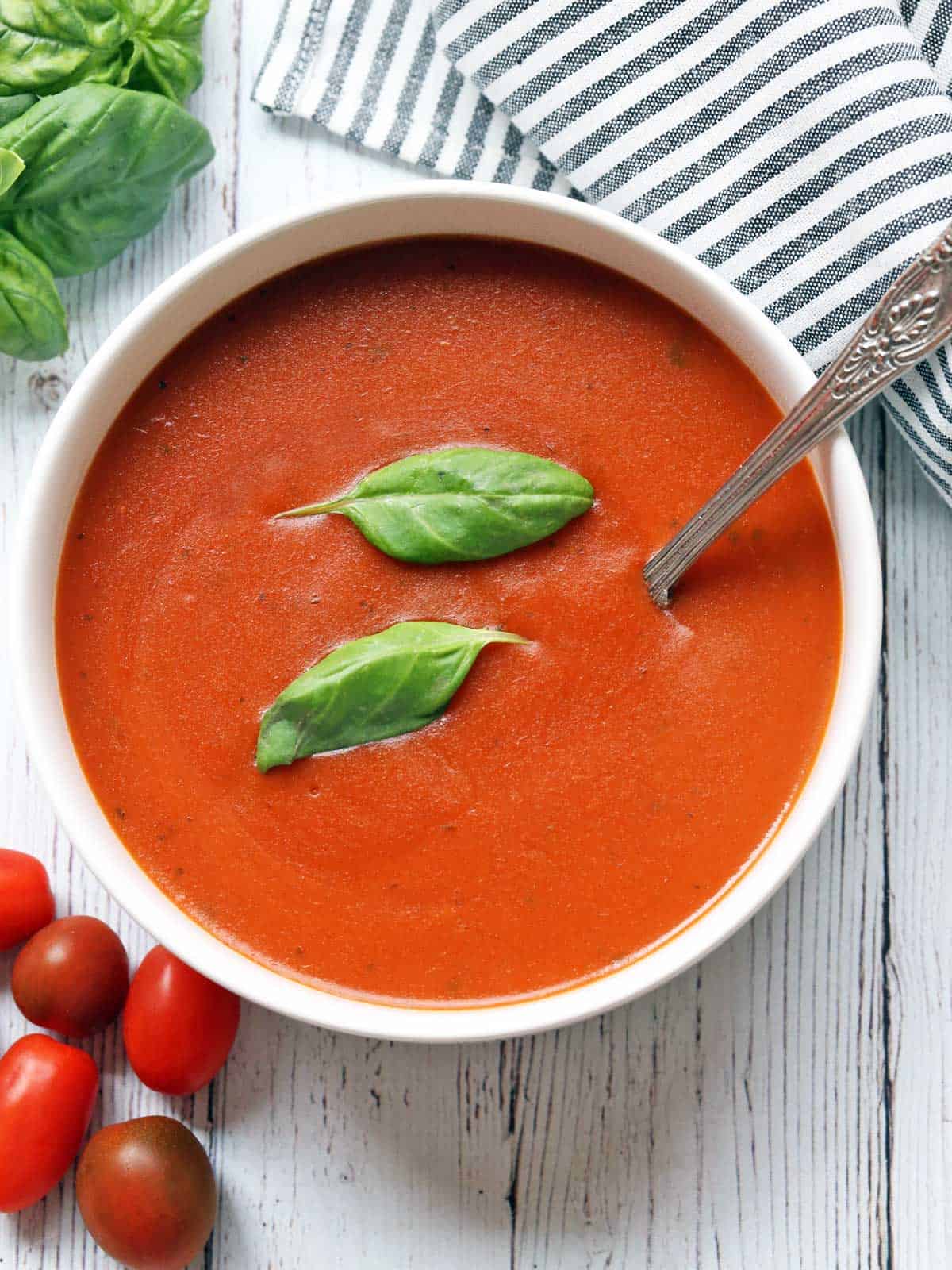 Tomato soup is served in a white bowl with a silver spoon. 