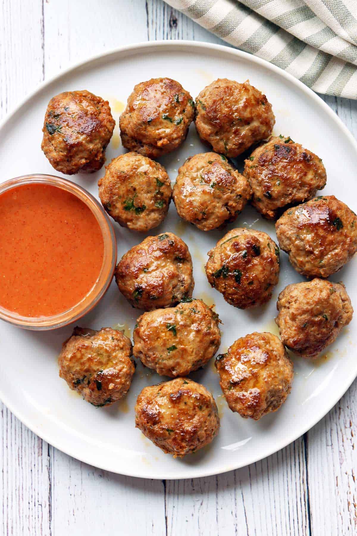 Turkey meatballs are served on a white plate with a dipping sauce and a napkin. 