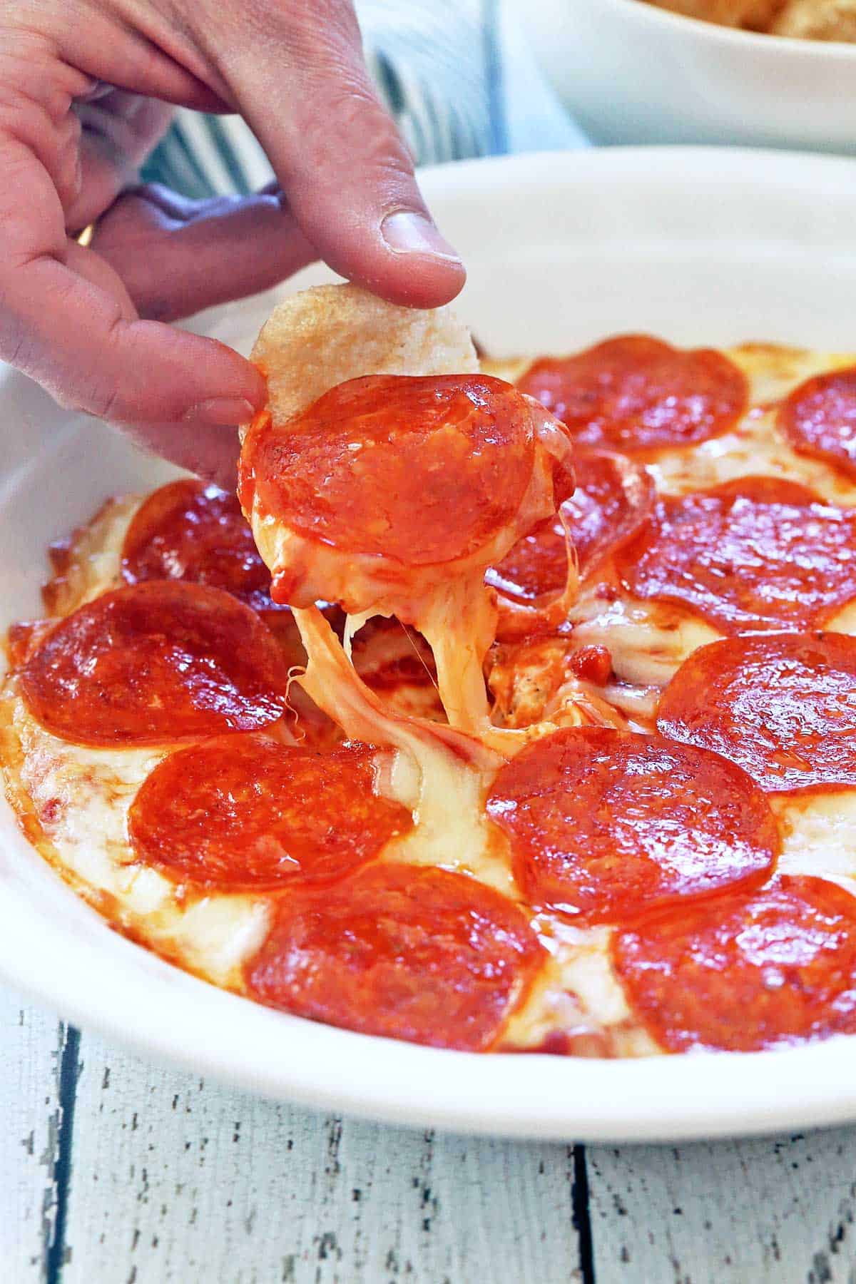 Pizza dip is served in a white baking dish and scooped with pork rinds.