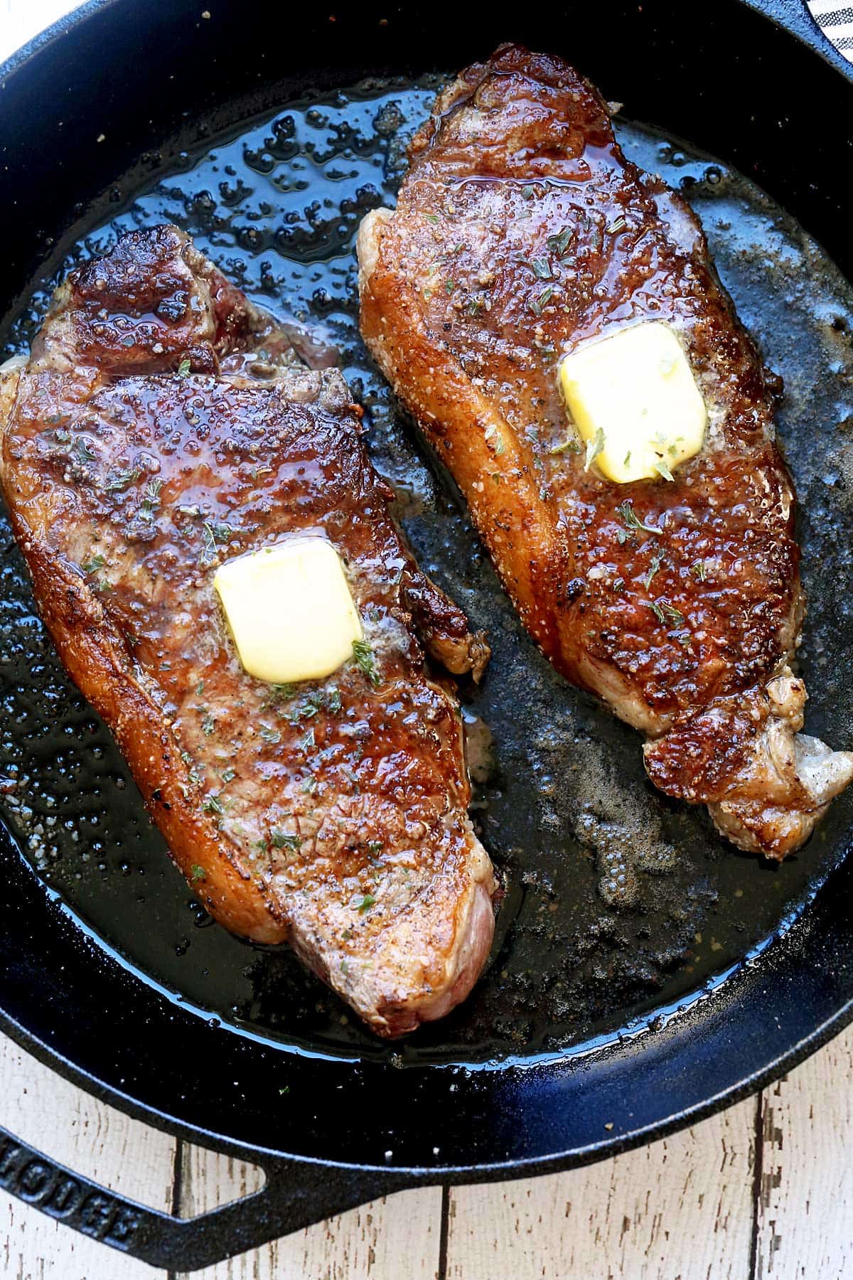 Two New York steaks are served in a cast-iron skillet and topped with butter. 