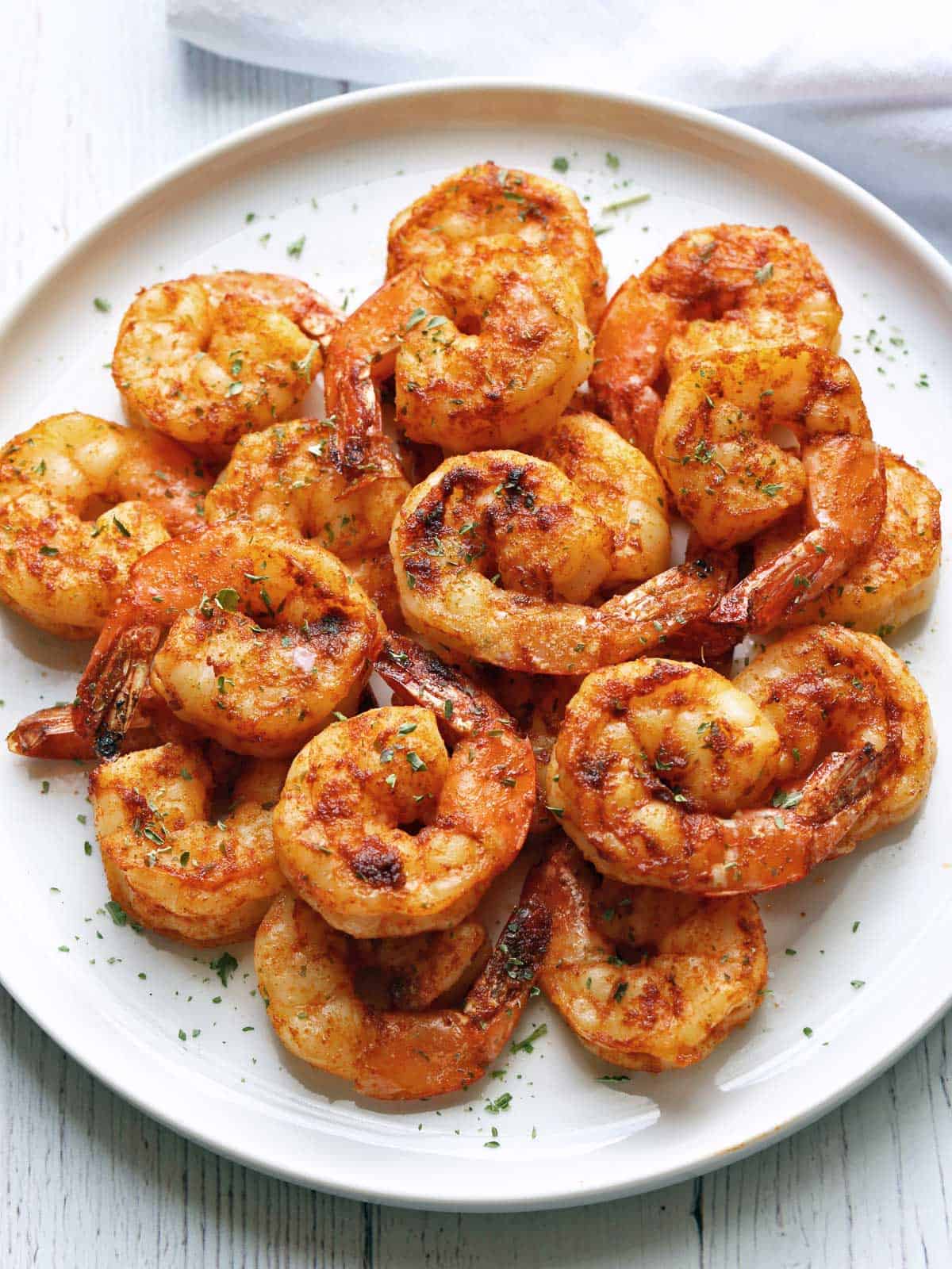 Broiled shrimp with cajun seasoning are served on a white plate.
