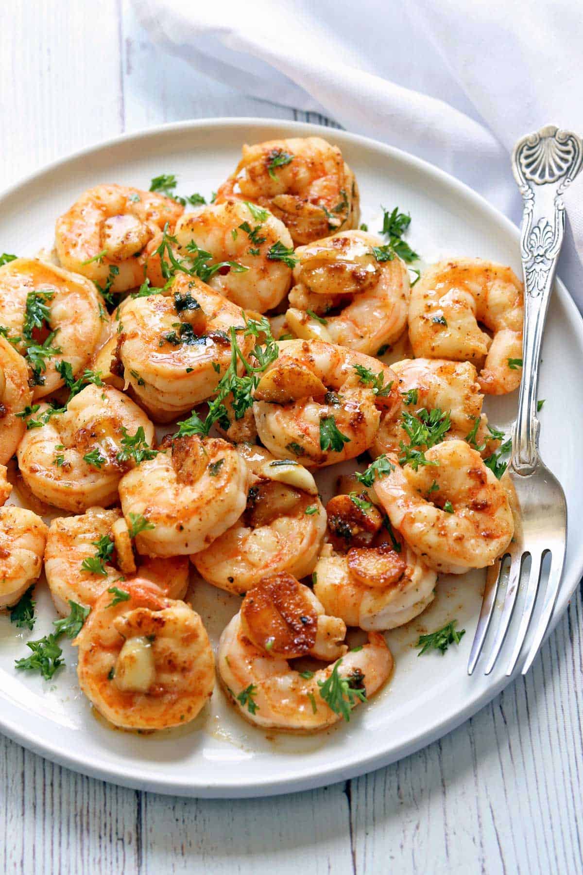 Garlic butter shrimp are served on a white plate with a silver fork. 