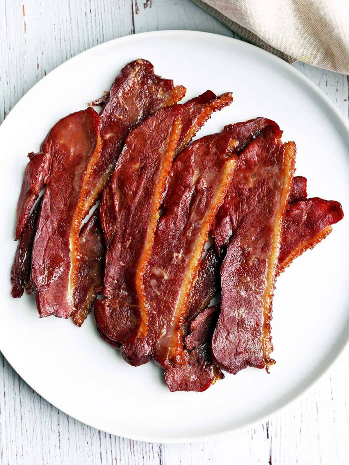 Duck bacon slices are served on a white plate.