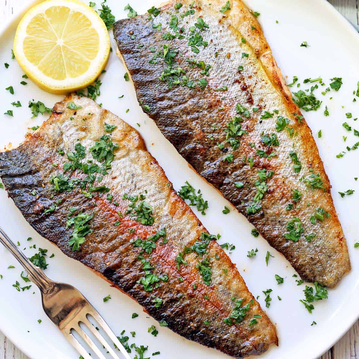 Rainbow trout fillets are served on a white plate with a fork.