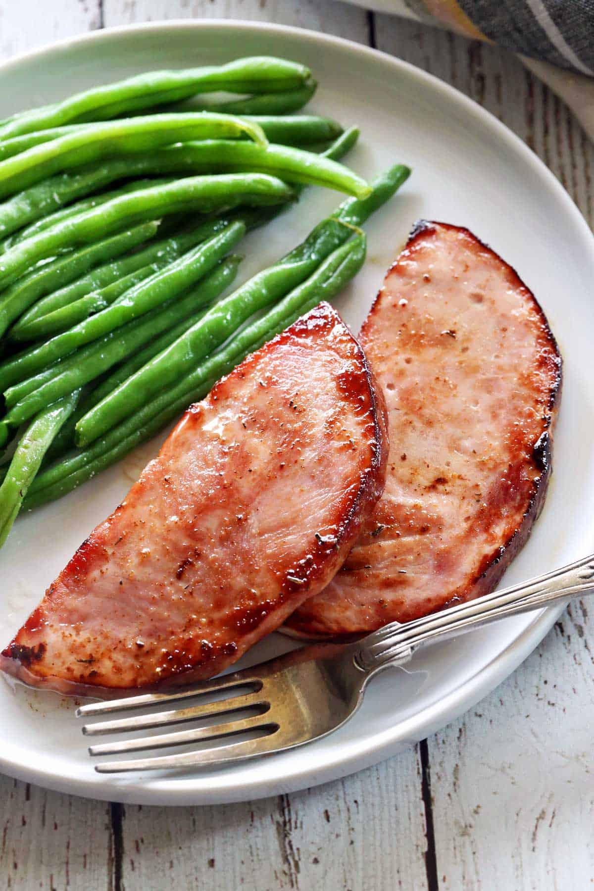 Ham steak is served with green beans.