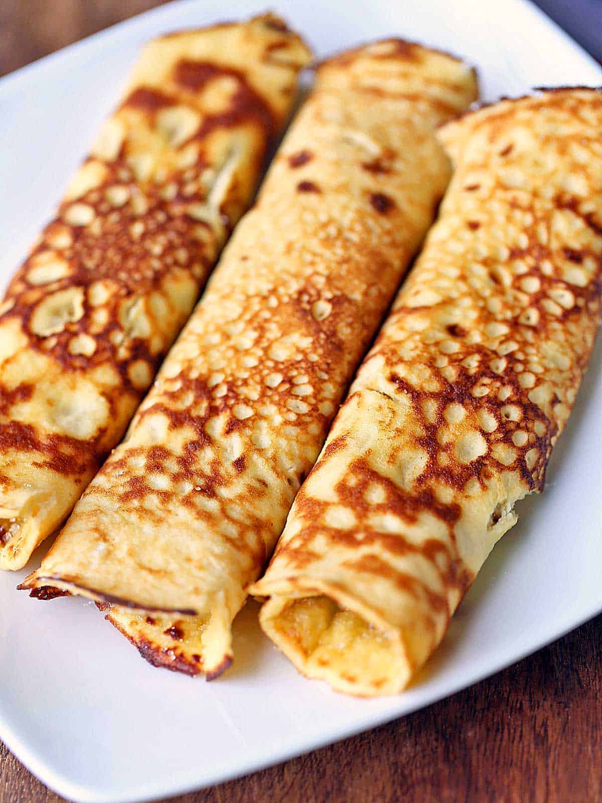 Three pannenkoeken are rolled up and served on a white plate. 