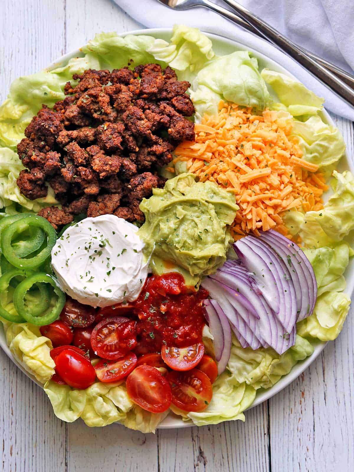 Keto taco salad is served on a white plate. 