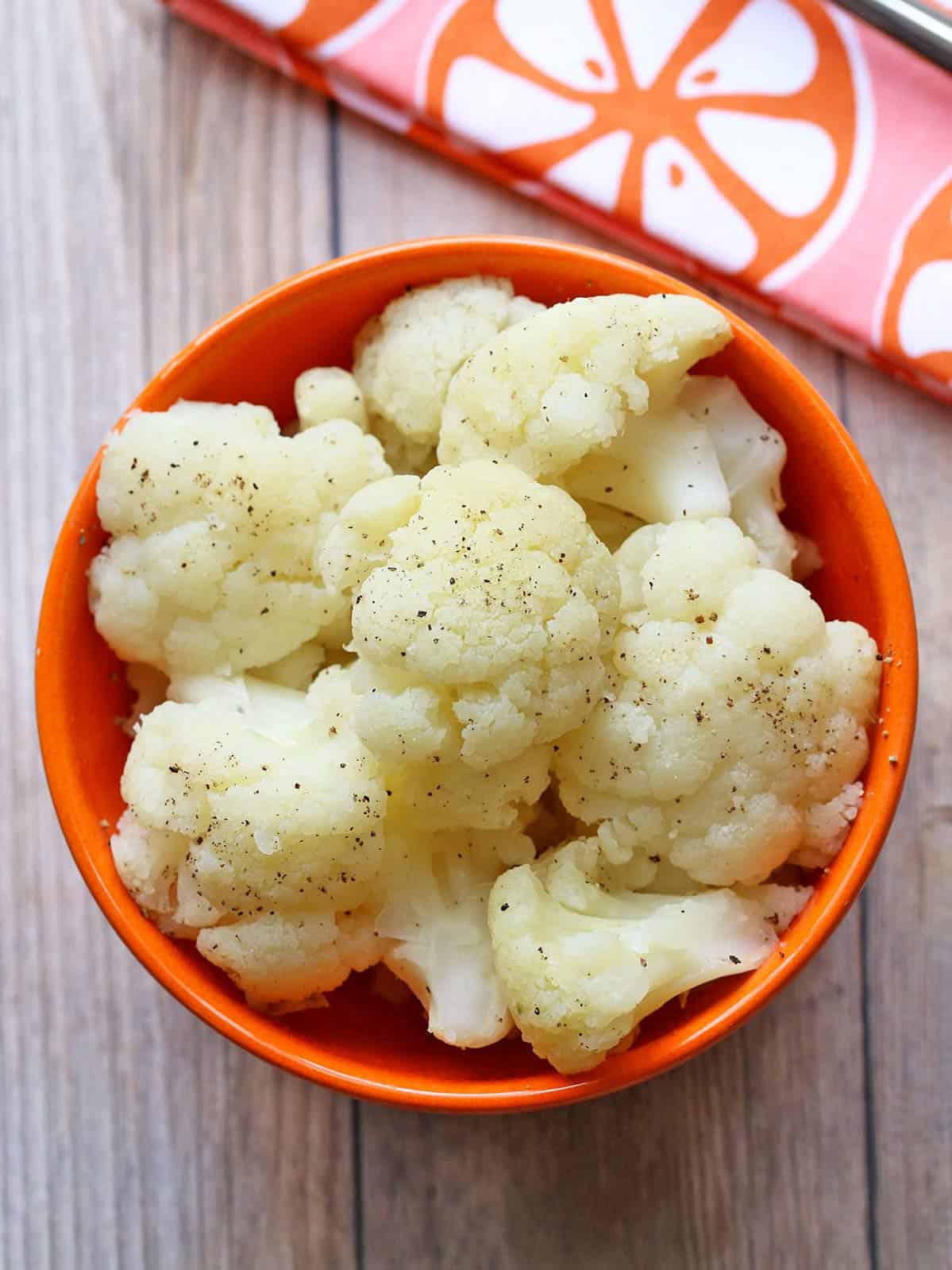 Microwave cauliflower florets are served in an orange bowl.
