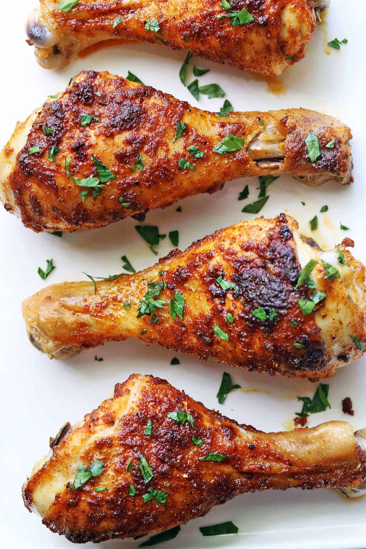Baked chicken drumsticks are topped with chopped parsley. 