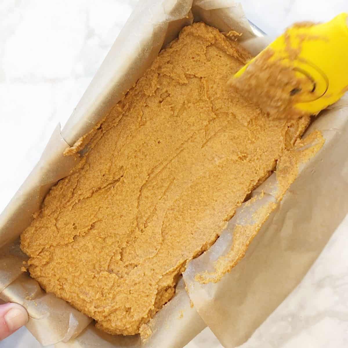 Smoothing out pumpkin bread batter in a loaf pan.