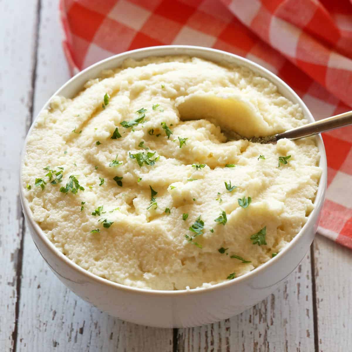 Mashed cauliflower made with frozen florets is served in a white bowl with a spoon.