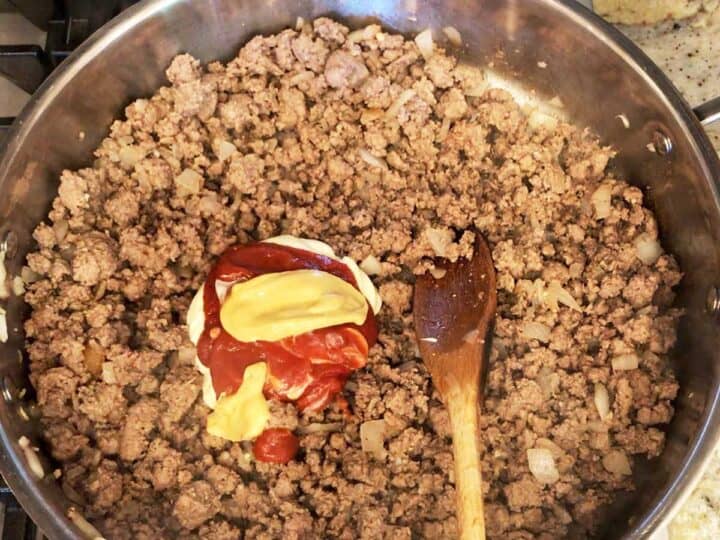 Stirring mayo, mustard, and ketchup into the beef mixture.