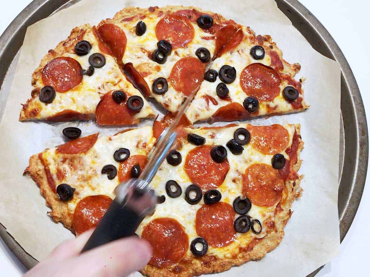 Cutting chicken crust pizza into slices. 
