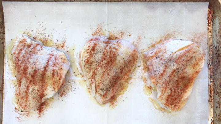 Seasoned raw chicken thighs on a baking sheet.
