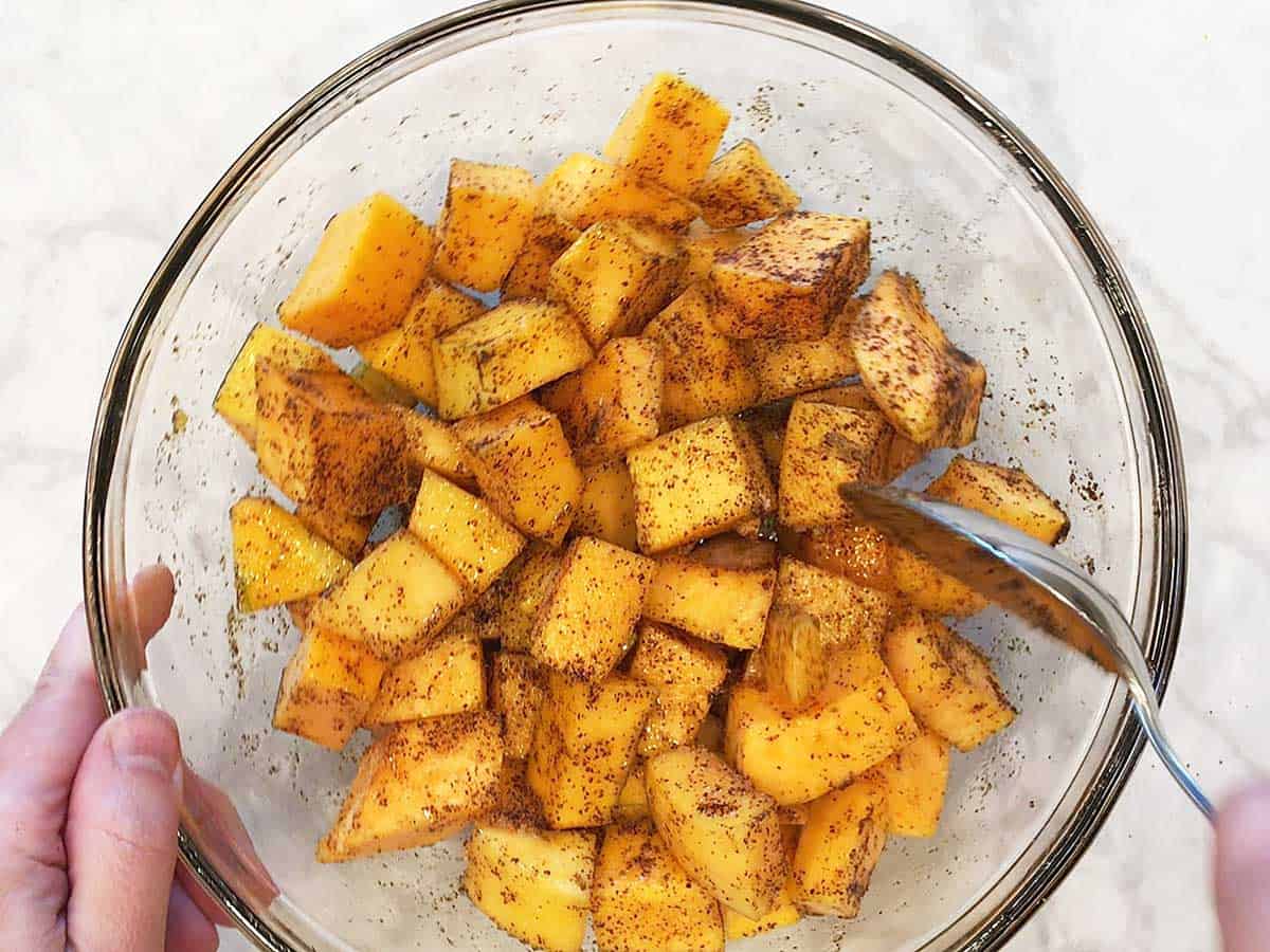 Using a spoon to coat the butternut squash in the spices.