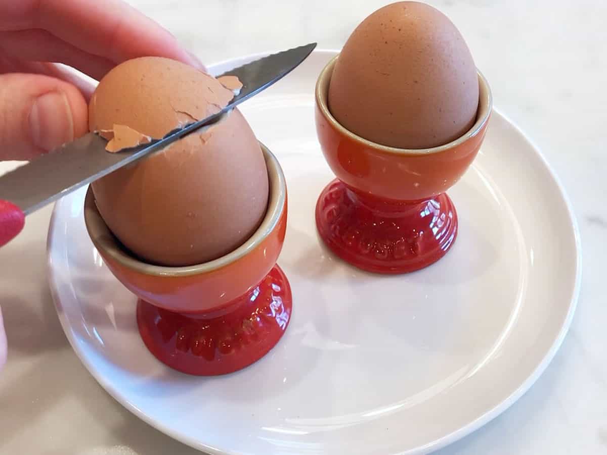 Slicing off the top of a soft-boiled egg with a knife.