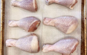 Raw drumsticks arranged on a baking sheet.