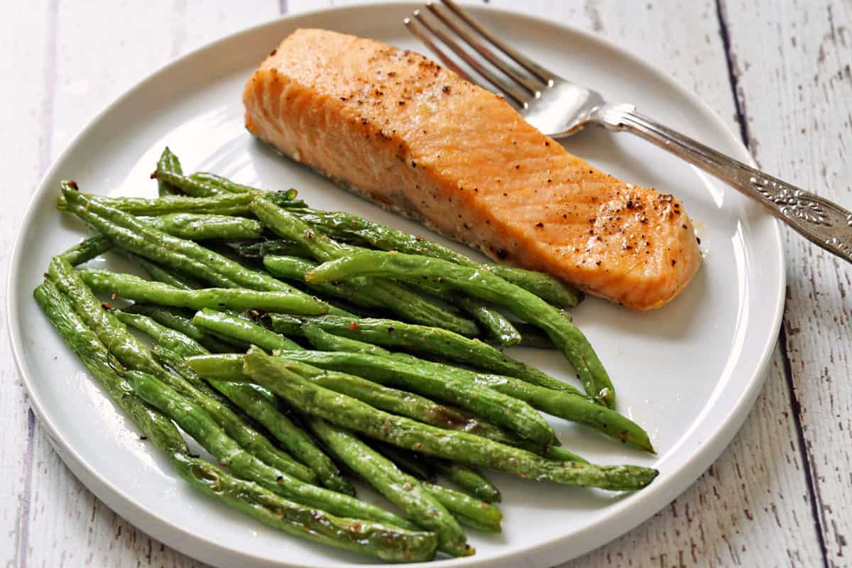 Baked salmon and roasted green beans on a white plate with a fork.